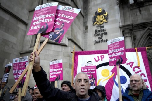 Stand Up To Racism campaigners hold banners outside the High Court in London, Monday, Dec. 19, 2022. Judges at Britain’s High Court say the U.K. government’s controversial plan to send asylum-seekers on a one-way trip to Rwanda is legal. But two judges also ruled that the government failed to consider the circumstances of the individuals it tried to deport. (AP Photo/Kirsty Wigglesworth)