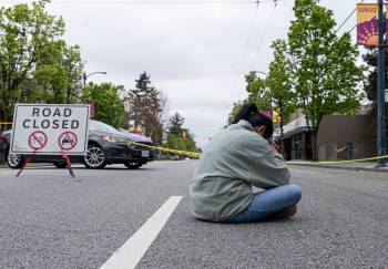 A woman sits and prays on Sunday near the site where a vehicle drove into a crowd at a street festival on Saturday in Vancouver, killing 11 people. (The Canadian Press)