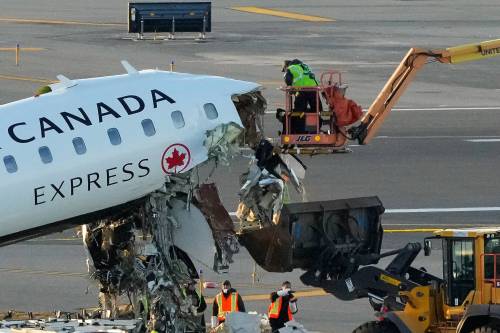 Aircraft maintenance workers in a boom lift cut away debris hanging from the wreckage of an Air Canada Express jet on Tuesday, just off the runway where it had collided with a Port Authority fire truck Sunday night at LaGuardia Airport in New York. (The Associated Press)